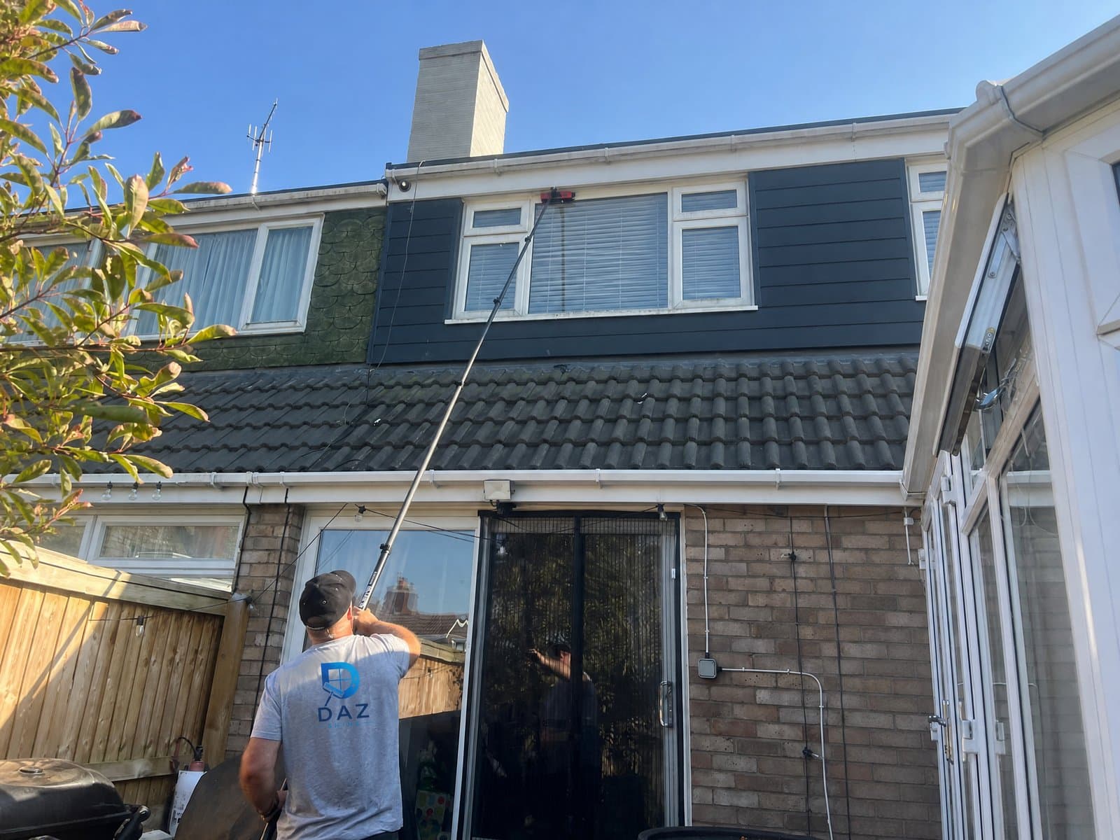 Darren from Daz Shine cleaning a Bristol home's windows with a water-fed pole, wearing his Daz Shine work shirt